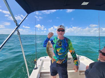 An angler proudly displaying a colorful Snapper while fishing on a boat in clear blue waters.