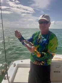 An angler proudly displaying a freshly caught fish while fishing on a boat in sunny waters.
