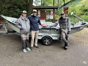 Three anglers pose beside a sleek fishing boat from Chrome City Guide Service, showcasing their readiness for a day on the water.