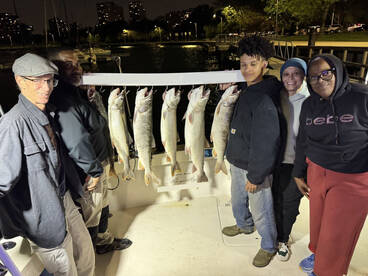 A group of anglers proudly posing with their catch of Lake Trout displayed on a board during a night fishing trip.