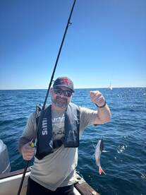 Angler proudly displaying a small fish while fishing on a boat in clear blue waters.