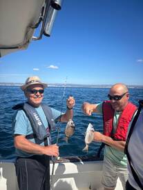 Two anglers proudly displaying their catches of Snapper while fishing on a sunny day.