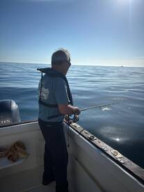 An angler casting a line from a boat in calm waters, enjoying a peaceful day of fishing under clear skies.