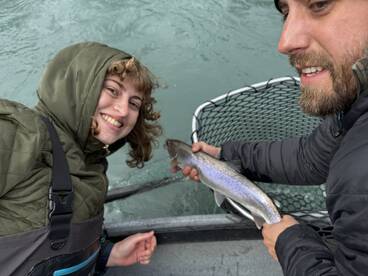 Two anglers smiling while showcasing a freshly caught Rainbow Trout during a fishing trip.
