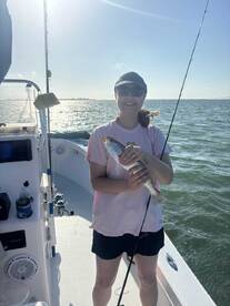 A happy angler holding a Speckled Trout while fishing on a sunny day, showcasing a successful catch on the boat.