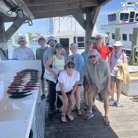 A cheerful group of anglers posing with their catch of redfish displayed on a board at the dock, showcasing a successful fishing trip.