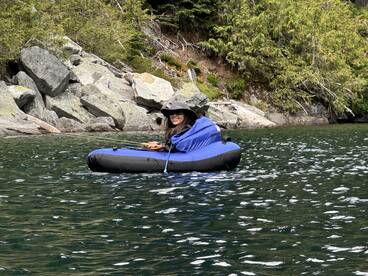A female angler enjoying a peaceful fishing experience in a blue inflatable boat surrounded by rocky terrain and lush greenery.