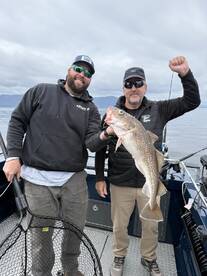 Two anglers proudly displaying a large Cod caught during a fishing trip on a boat.