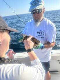 An angler is engaged in tagging a fish while fishing on a boat, showcasing a hands-on conservation effort in a sunny marine environment.