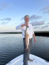 Angler proudly displaying a large Redfish while standing on the bow of a boat during a serene fishing trip.