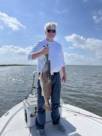 An angler proudly displaying a large Redfish while standing on a boat in a sunny fishing environment.