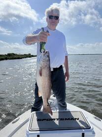 Angler proudly displaying a large Redfish while standing on a Sportsman boat in a scenic waterway.