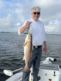 A proud angler holding a large Redfish while standing on a boat in a scenic fishing environment.