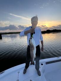 An angler proudly displaying a large Redfish at sunset while standing on the boat, showcasing a successful fishing trip.