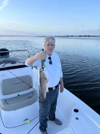 An angler proudly displaying a freshly caught Redfish while standing on a boat in calm waters.