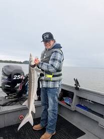 Angler proudly displaying a Sturgeon while fishing from a boat in a calm water setting.
