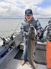 Excited angler holding a large Sturgeon on a fishing boat, showcasing a successful catch during a day on the water.