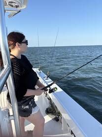 A young woman is casting her line while fishing on a boat in open water, enjoying a sunny day on the Gulf Coast.