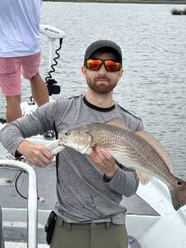 Angler proudly displaying a Redfish while fishing on a boat in a calm waterway.