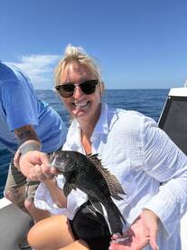 A happy angler proudly displaying a Black Sea Bass while fishing on a sunny day.