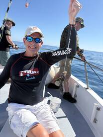 A smiling angler proudly displaying his catch while fishing on a boat, with another fisherman in the background.