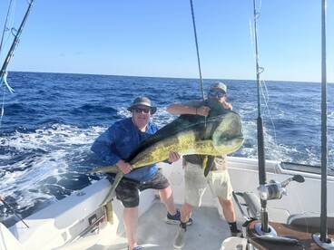 Two anglers proudly displaying a large Mahi-Mahi while fishing offshore, showcasing a successful day on the water.