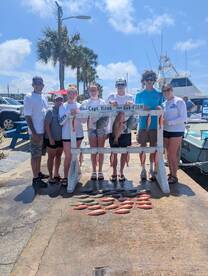 A group of young anglers proudly displaying their catch of Snapper and Grouper on a catch board after a successful fishing trip.