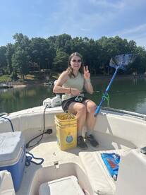 A young woman enjoying a fishing trip on a boat, holding a fishing rod and smiling while surrounded by a scenic lake view.