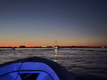 A scenic view of the boat's bow at sunset, showcasing the tranquil waters and distant fishing vessels, perfect for evening fishing trips.
