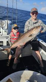 A young angler and his father proudly display a large Amberjack while fishing offshore, showcasing a memorable family fishing experience.