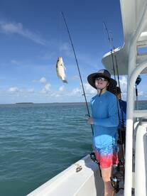 A young angler proudly displaying a caught fish while fishing on a boat in clear blue waters.