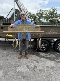 An angler proudly displaying a catch of several fish on a wooden board, showcasing a successful fishing trip with Doty Outdoors.