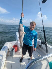 Angler proudly displaying a large Redfish while fishing on a boat in open waters.