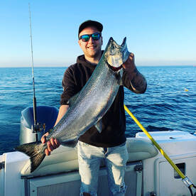 Angler proudly displaying a large Salmon while fishing on a calm day at sea.