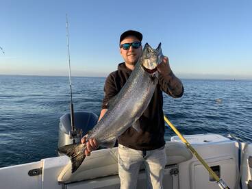 Angler proudly displaying a large Salmon while fishing on a boat in open waters.