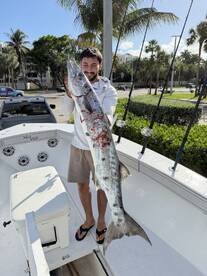 Angler proudly displaying a large Barracuda on a fishing boat, showcasing a successful day on the water.