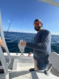 Angler proudly displaying a freshly caught fish while fishing offshore, with a clear blue sky in the background.