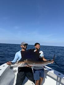 Two anglers proudly displaying a large Sailfish on a fishing boat, showcasing a successful deep-sea fishing trip.