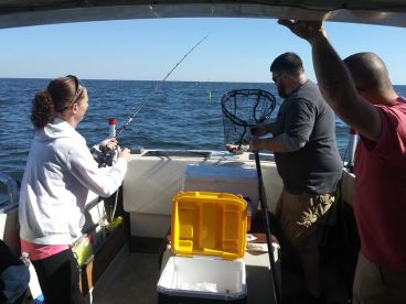 A group of anglers actively fishing on a boat, with one person reeling in a catch while another prepares a net, showcasing a lively fishing experience.