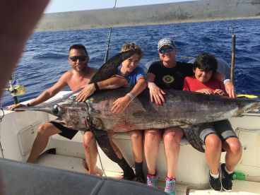 A family proudly displays a large Swordfish aboard their boat during a deep-sea fishing trip.