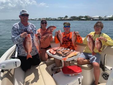 A family proudly displaying their catch of Red Snapper aboard a boat, showcasing a successful fishing trip in a coastal setting.