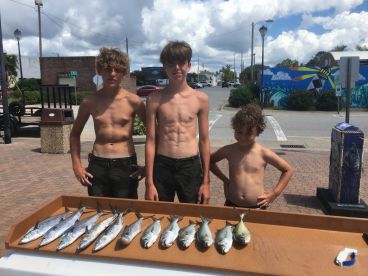 Three young anglers proudly displaying their catch of fish on a board, showcasing their successful day of fishing.