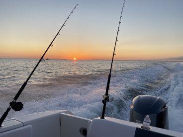 A scenic view of a boat heading out to sea at sunset, with fishing rods positioned for a day of angling.