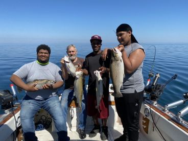 A group of anglers proudly displaying their catch of trout and other fish aboard a fishing boat on a clear day.