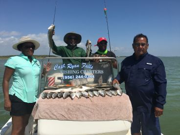 Group of anglers proudly displaying their catch of Speckled Trout on a fishing charter in a coastal environment.