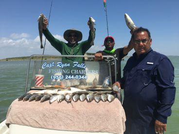 Three anglers proudly displaying their catch of Speckled Trout on a fishing charter in a coastal waterway.