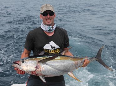 An angler proudly displays a large Yellowfin Tuna while out on the open ocean, showcasing a successful deep-sea fishing trip.