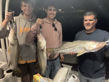 Two young anglers and an adult proudly displaying their catch of three large Snook on a night fishing trip.