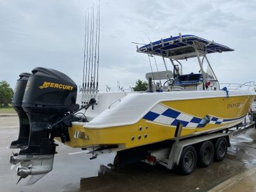 A sleek yellow Donzi boat equipped with twin Mercury engines and multiple fishing rods, parked on a trailer, ready for a fishing adventure.