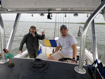 Two anglers inside a center console boat, preparing for a fishing trip on a calm waterway.